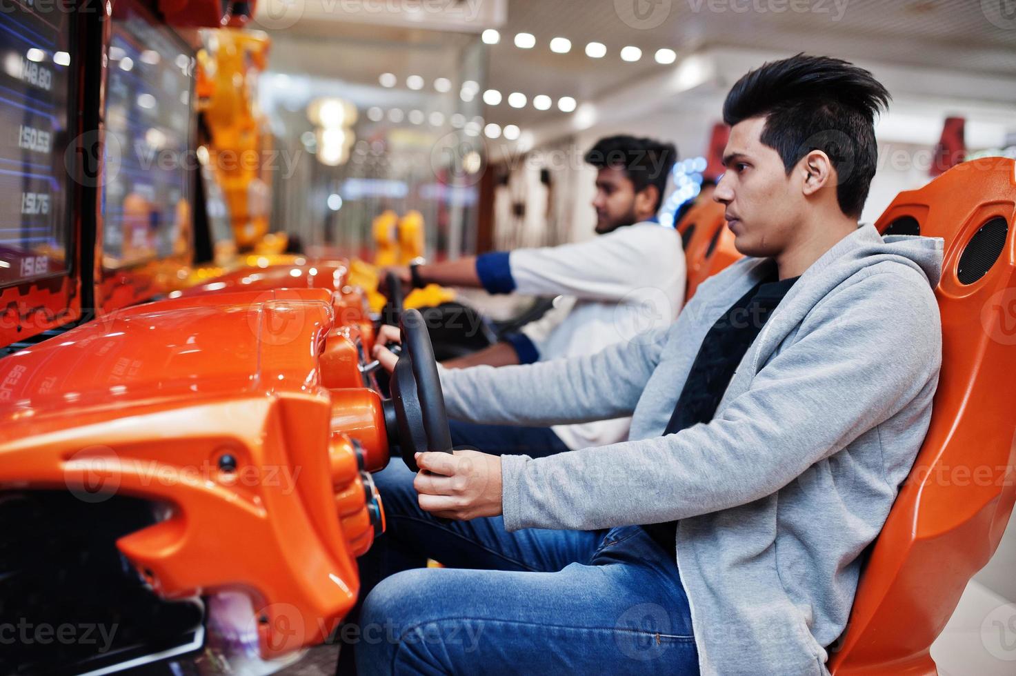 Two asian guys compete on speed rider arcade game racing simulator machine. photo