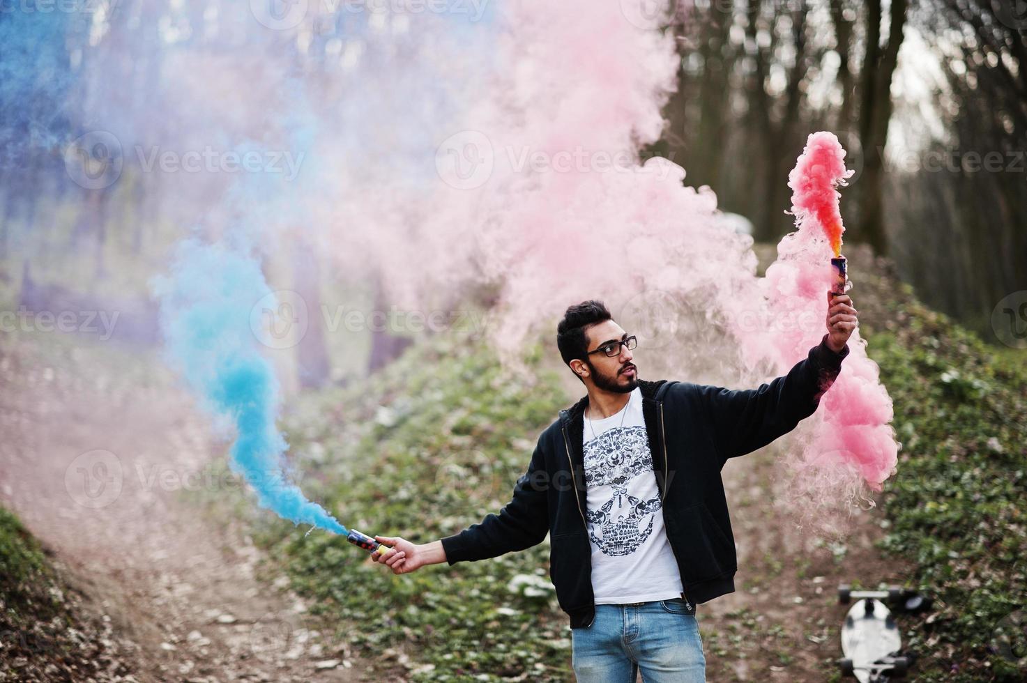 Street style arab man in eyeglasses hold hand flare with red and blue smoke grenade bomb. photo