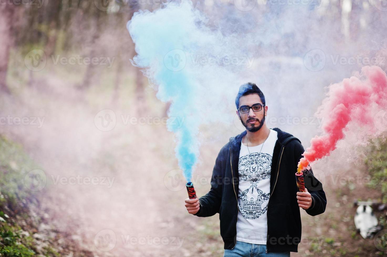 Street style arab man in eyeglasses hold hand flare with red and blue smoke grenade bomb. photo