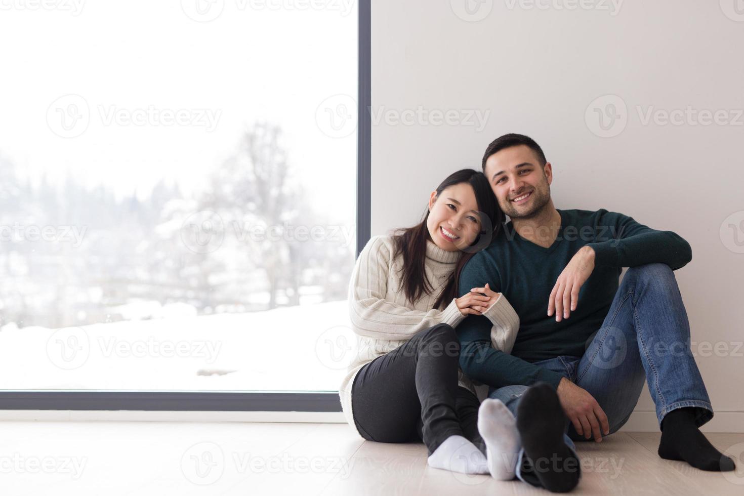 pareja multiétnica sentada en el suelo cerca de la ventana en casa foto