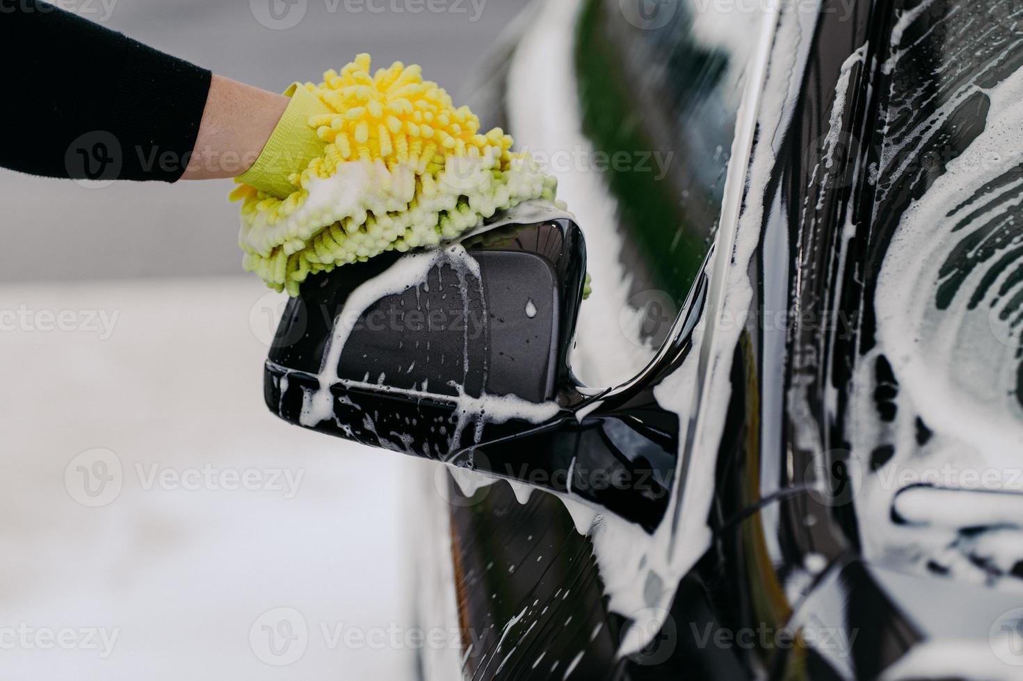 mans mano sujetando una esponja para lavar el coche. auto negro con pompas de jabón. concepto de limpieza. trabajador limpiando automovil foto