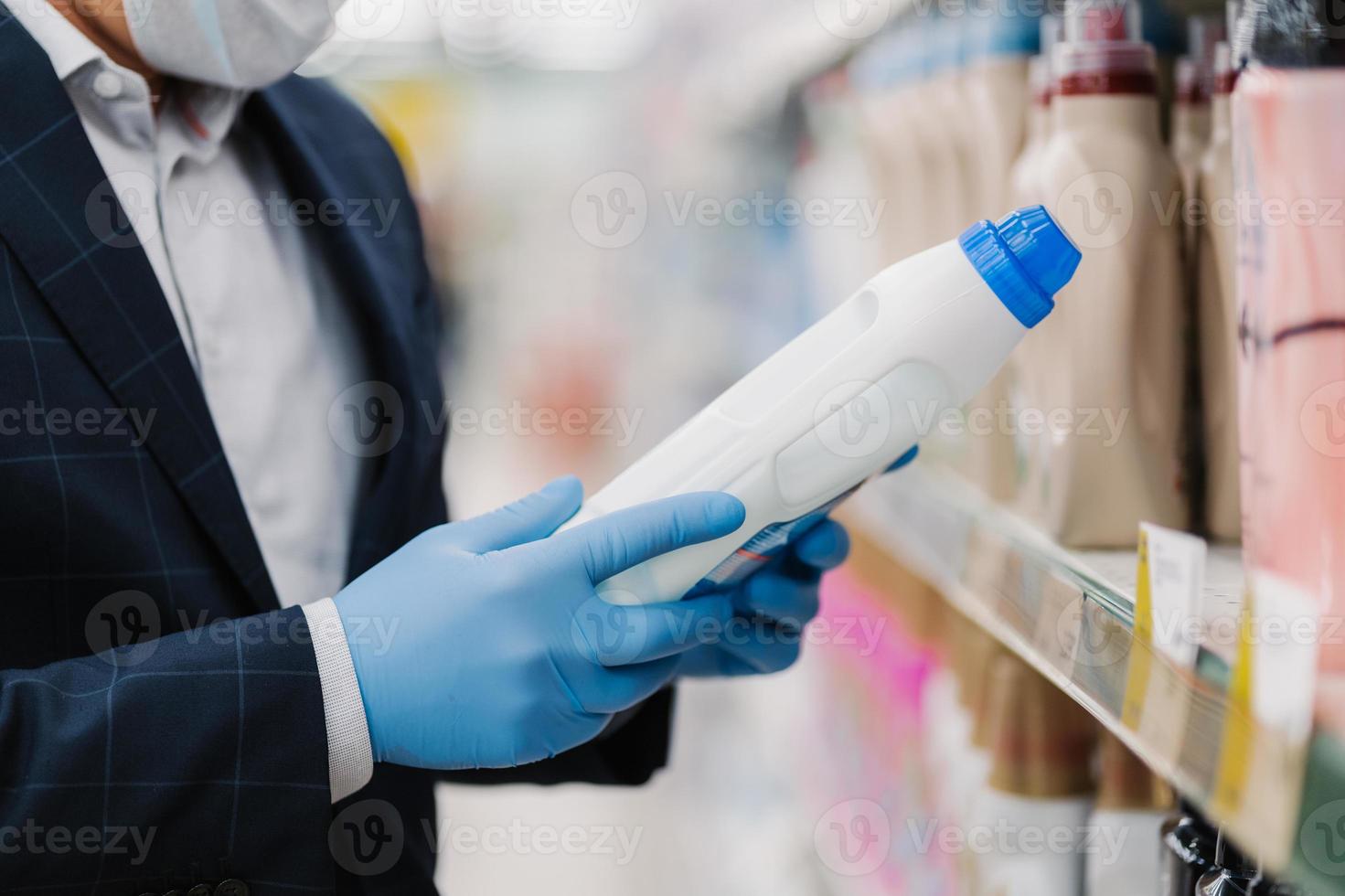 Unknown man wears protective rubber gloves, chooses household chemicals, selects washing powder in store, poses in department of cleaning product, protects from virus. Coronavirus and quarantine photo