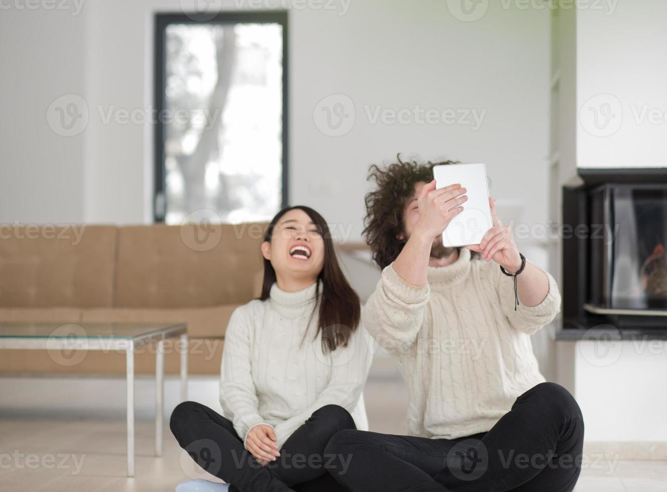 multiethnic couple using tablet computer in front of fireplace photo