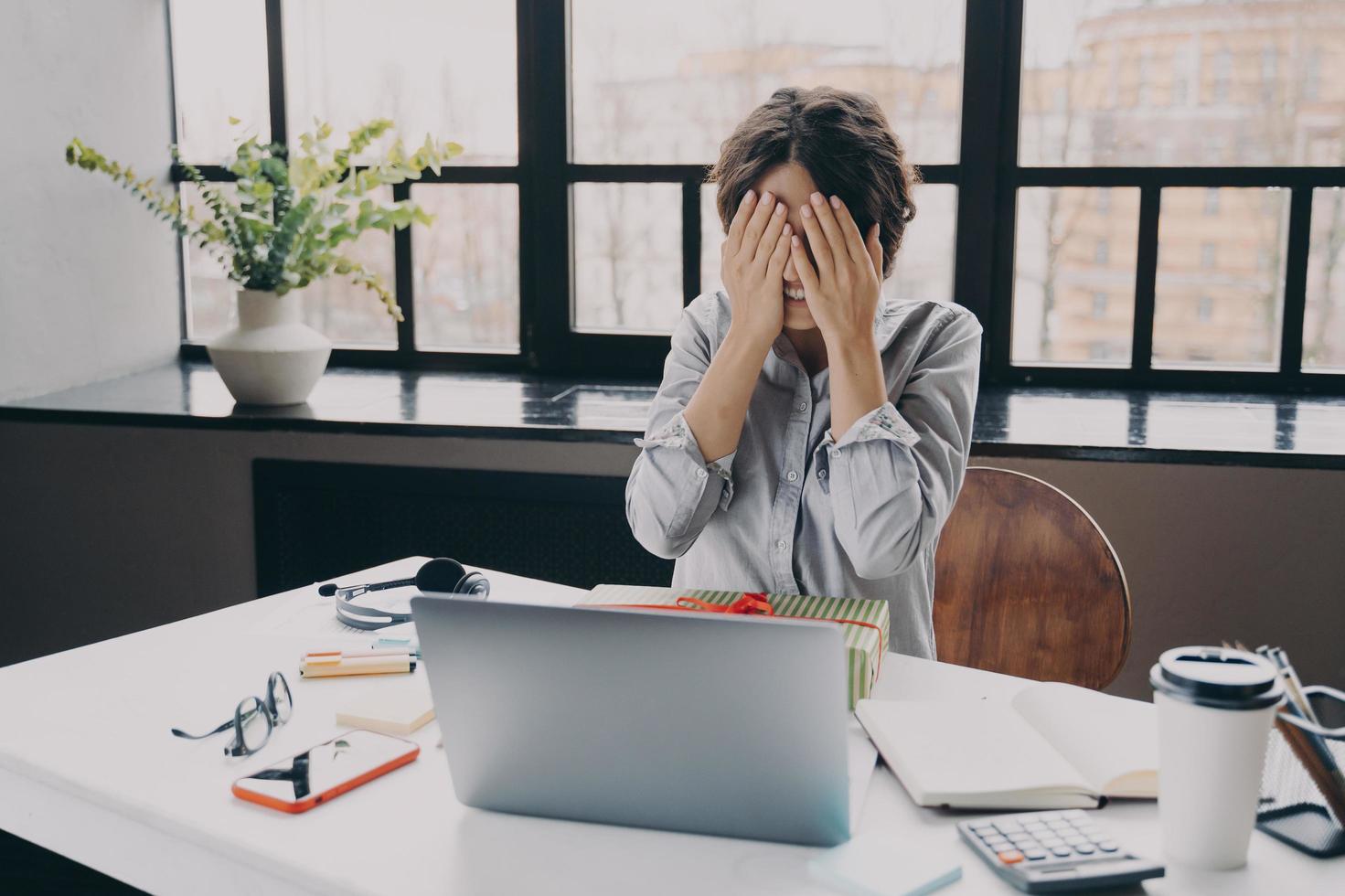 Curious woman office employee covering eyes with hands while getting x-mas present at work photo