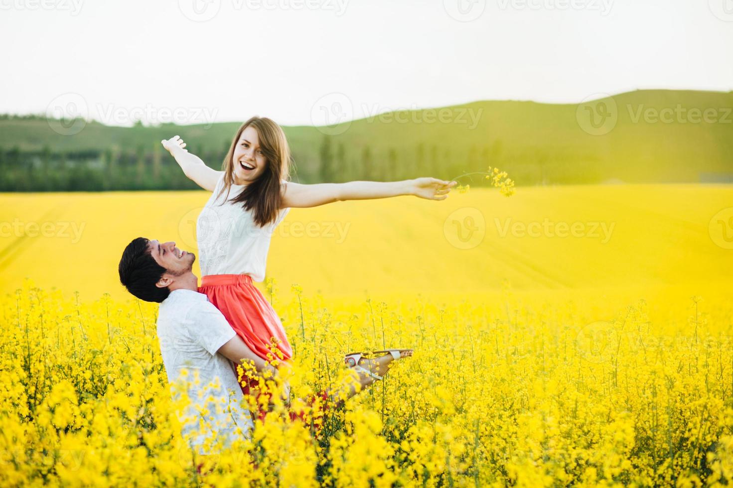 el hombre romántico cría a su novia, disfruta de la unión en el hermoso campo amarillo, posa al aire libre, se divierte, sonríe alegremente. pareja enamorada pasa las vacaciones de verano en la naturaleza. concepto de personas y armonía foto