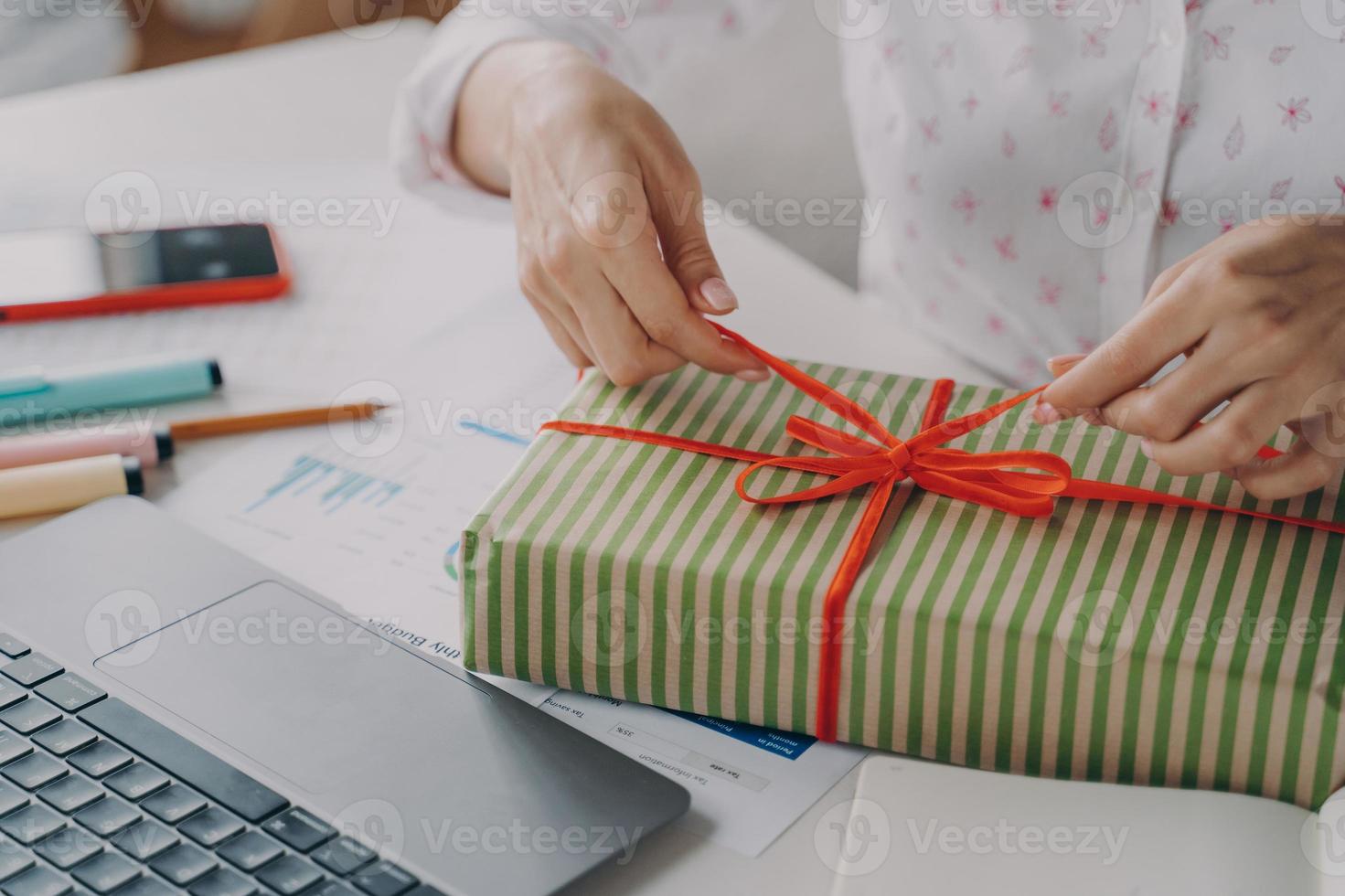 imagen recortada de una joven oficinista decora un regalo de navidad, sentada en el lugar de trabajo foto