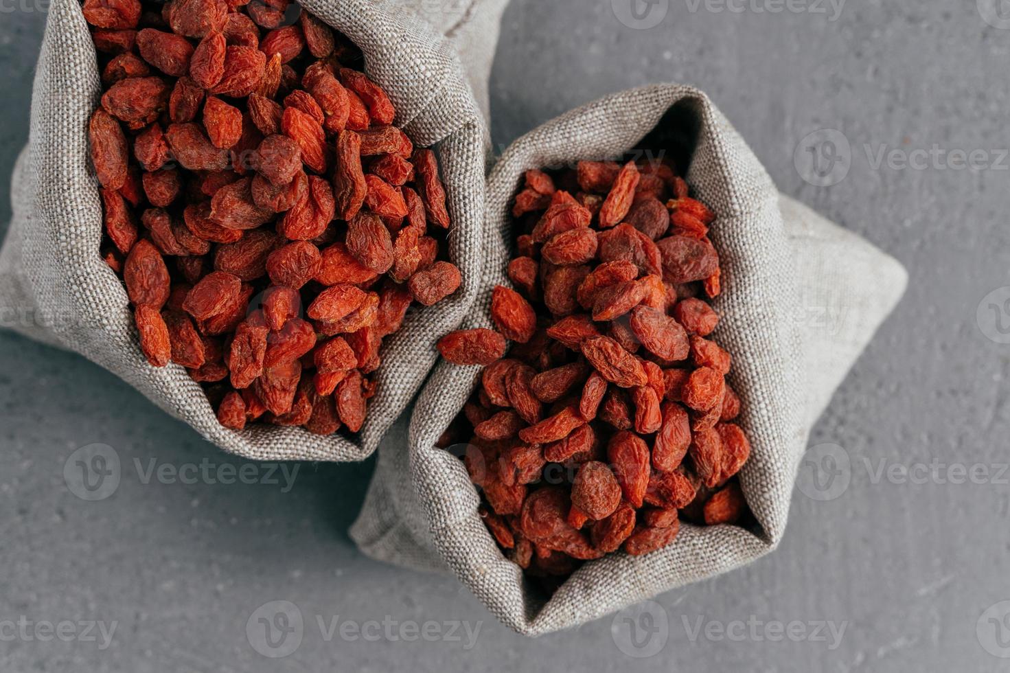 bayas de goji superalimento seco para una alimentación saludable en dos sacos de arpillera aislados sobre fondo gris. suplemento alimenticio. bayas de goji rojas en bolsas foto