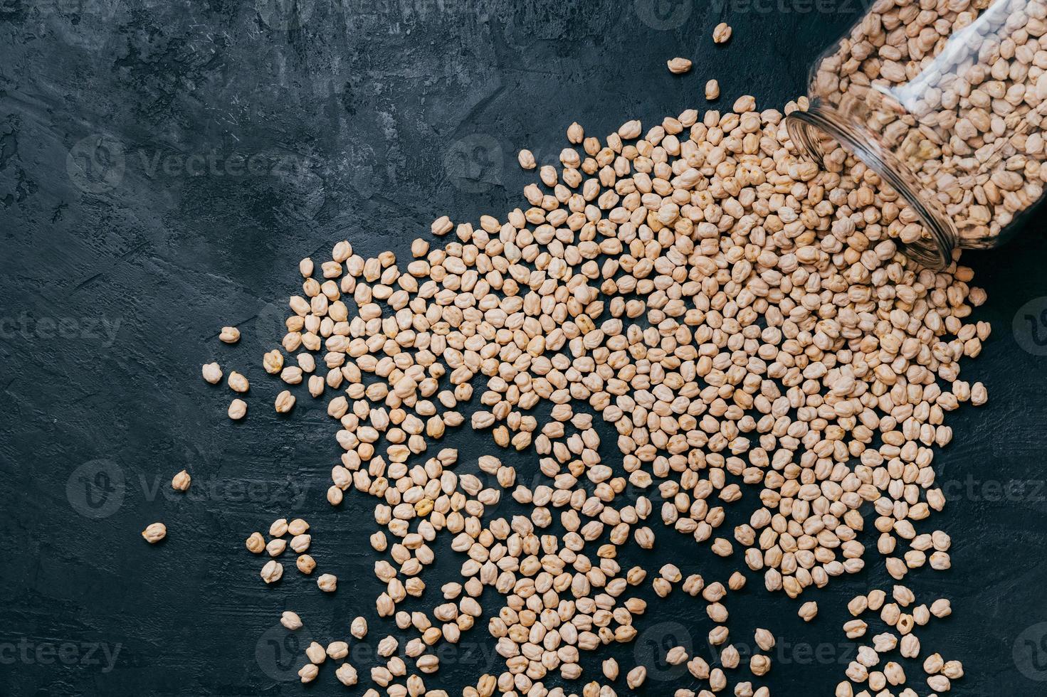 Healthy food, dieting and nutrition concept. Dry uncooked chickpeas spilled from glass jar on dark background. Vegan protein. Vegetarianism concept photo