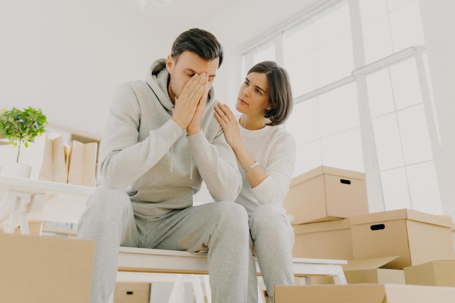 foto de marido y mujer insatisfechos obligados a vender apartamento debido a problemas financieros, la mujer calma al marido, posan en cajas de cartón, posan en la sala de estar. mudarse como una especie de estrés para la familia