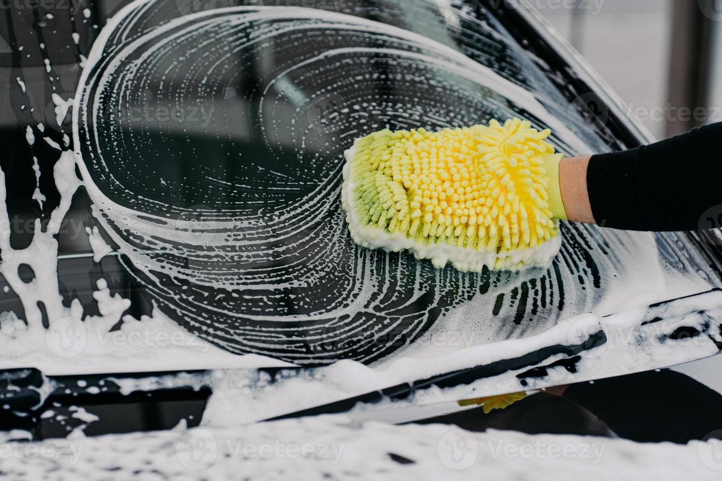 Car service concept. Unrecognizable man washes auto with cloth and car wash shampoo, has desire to cleanliness. Hand washing vehicle with sponge photo