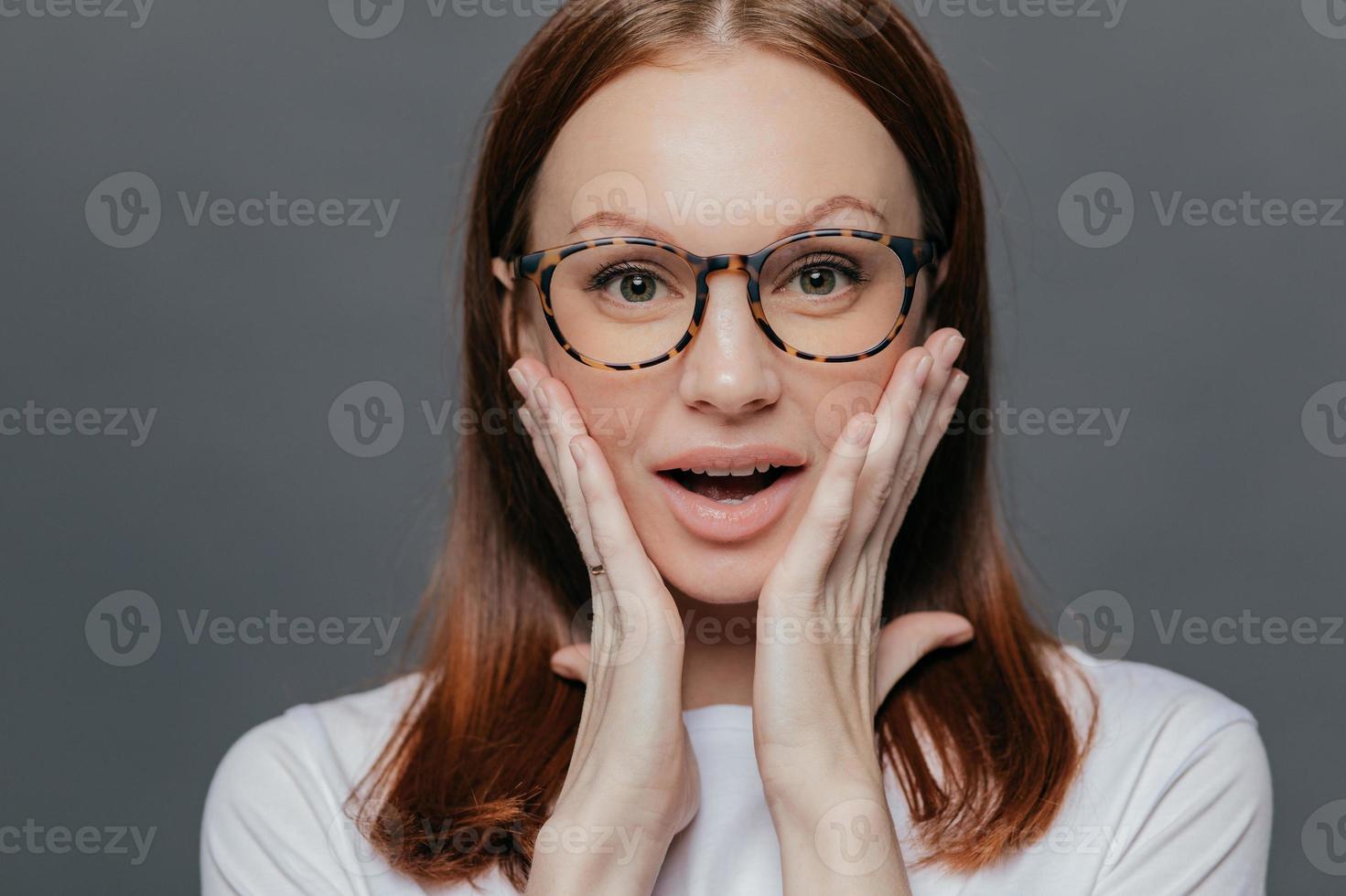 Headshot Of Surprised Young Caucasian Lady Keeps Both Palms On Her Cheeks Looks With Amazement Recieves Unexpected News Wears Spectacles White Clothing Poses Alone Against Grey Background Stock Photo At Vecteezy