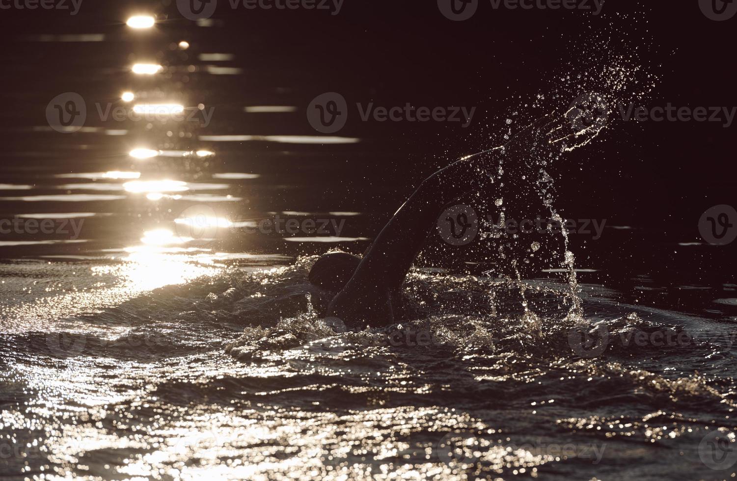 triathlon athlete swimming on lake in sunrise  wearing wetsuit photo