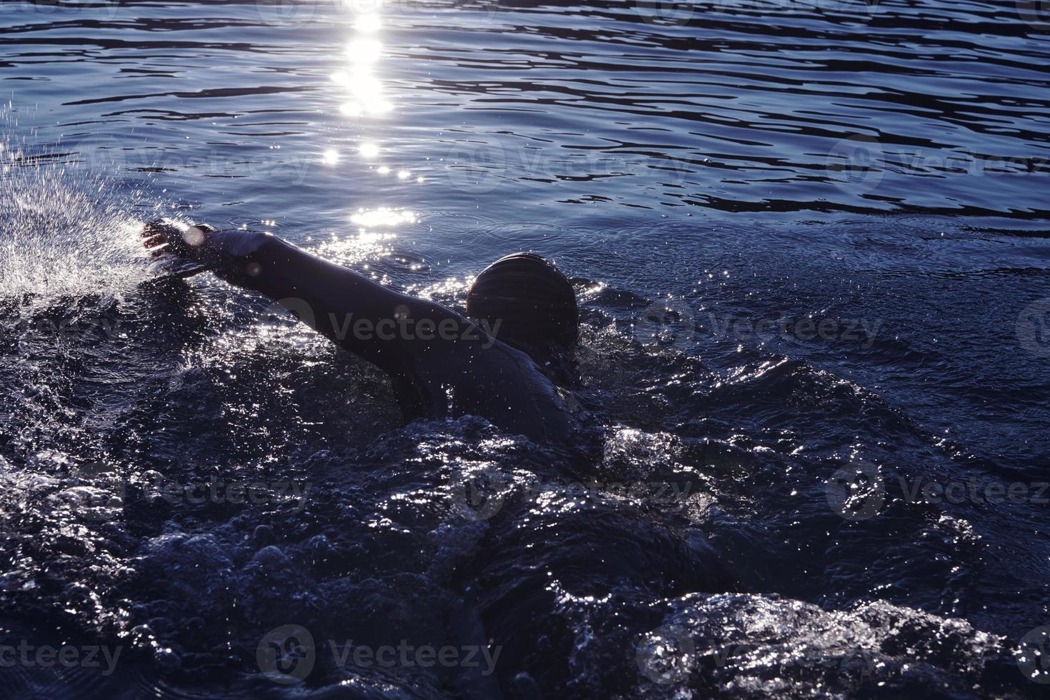 triathlon athlete swimming on lake in sunrise  wearing wetsuit photo