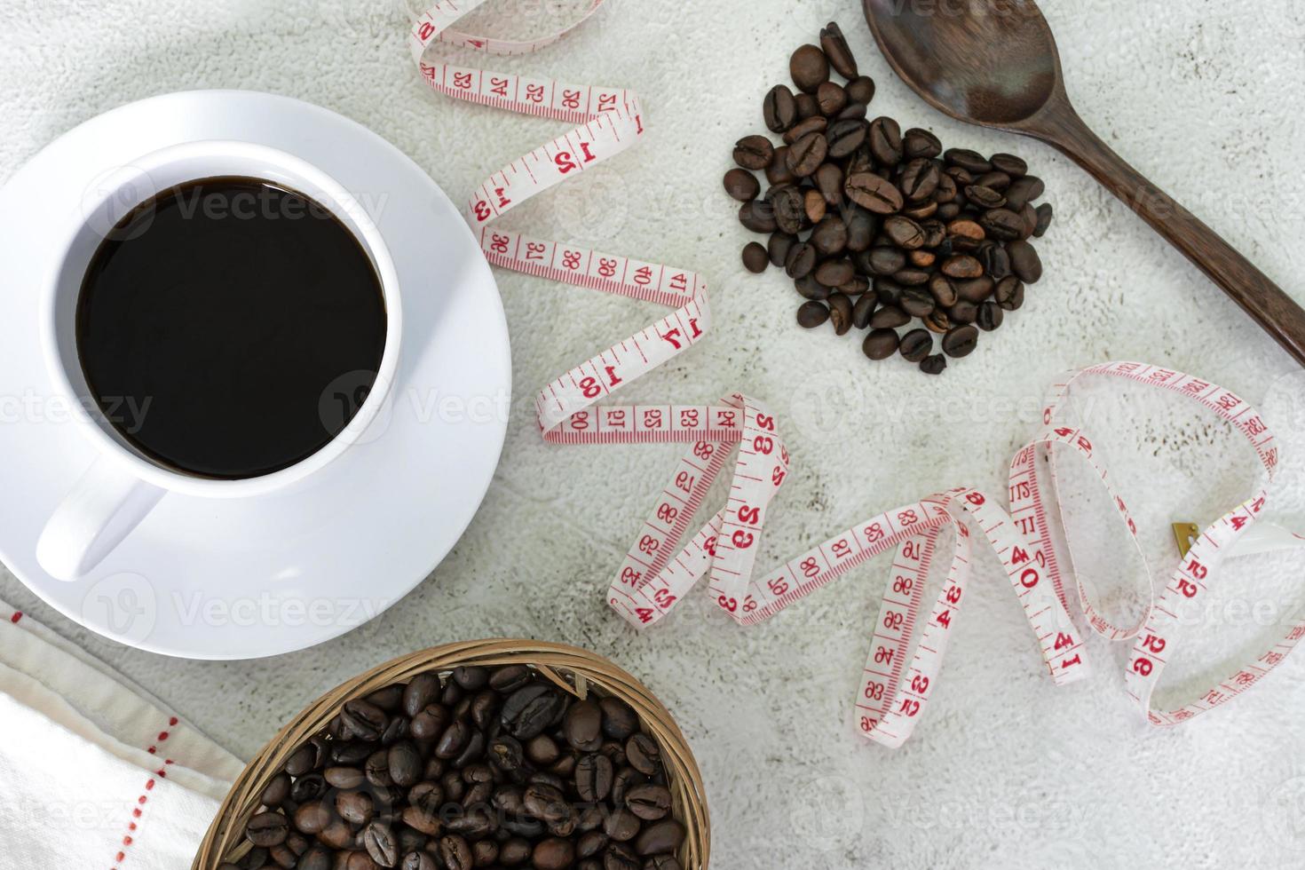 Cup of coffee and coffee beans background with measure tap on white desk. photo