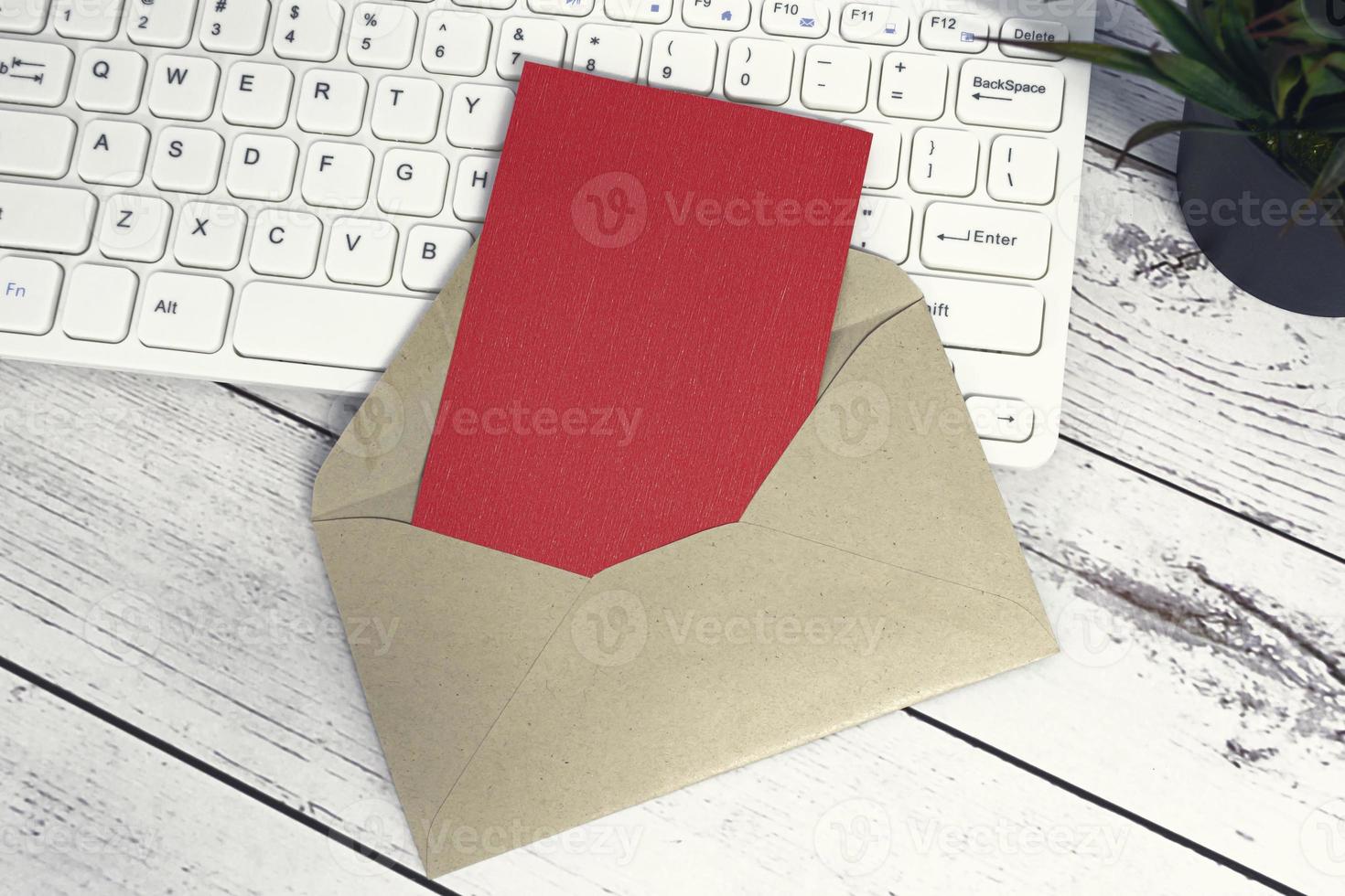 Red note inside brown envelope with keyboard and potted plant on wooden desk. photo