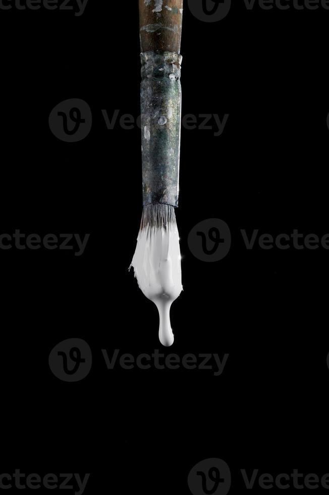 Paint brush with white colour isolated on black background. White paint drips from the brush. Photo with copy space. An old art brush.