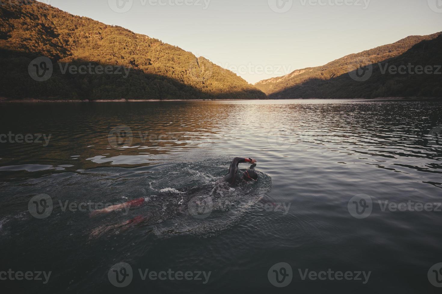 triathlon athlete swimming on lake in sunrise  wearing wetsuit photo
