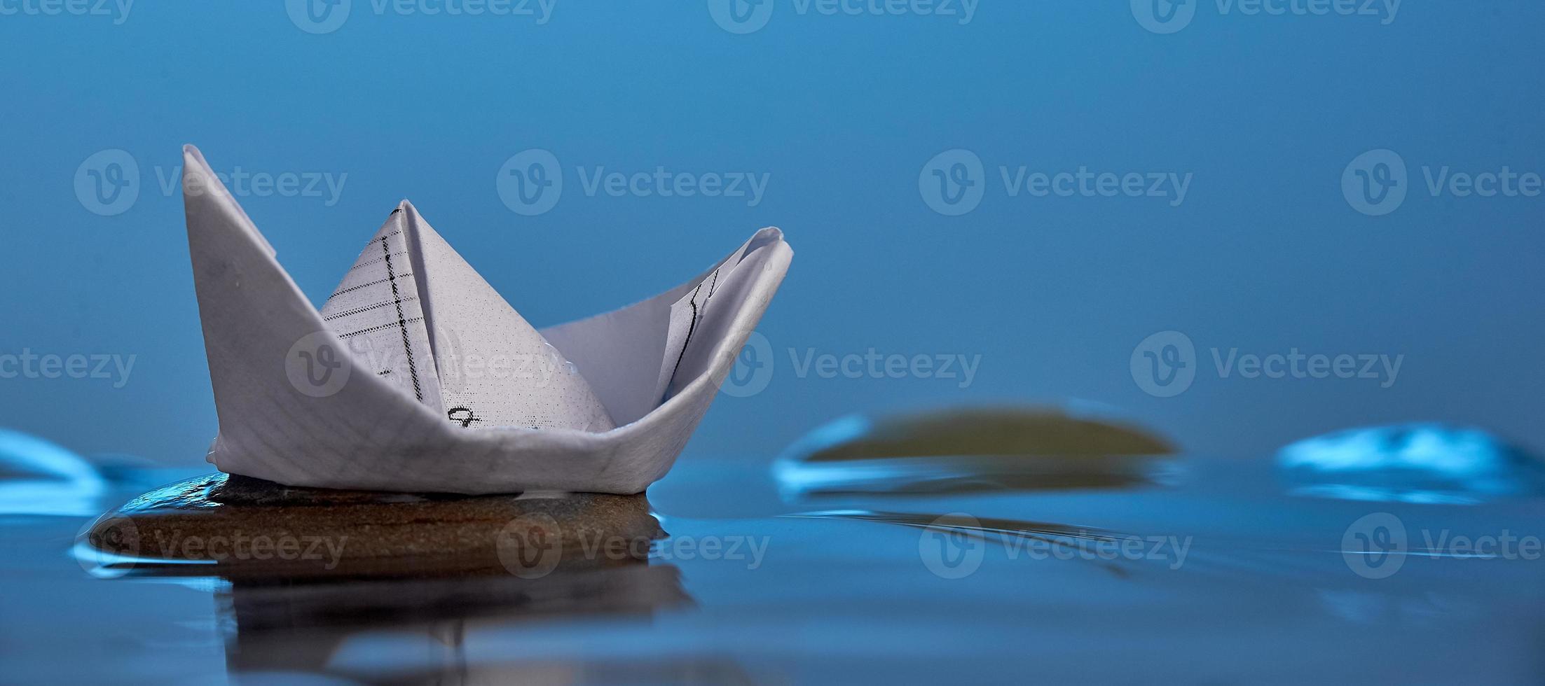 Paper origami boat on the stone in blue water. Photo with copy space.