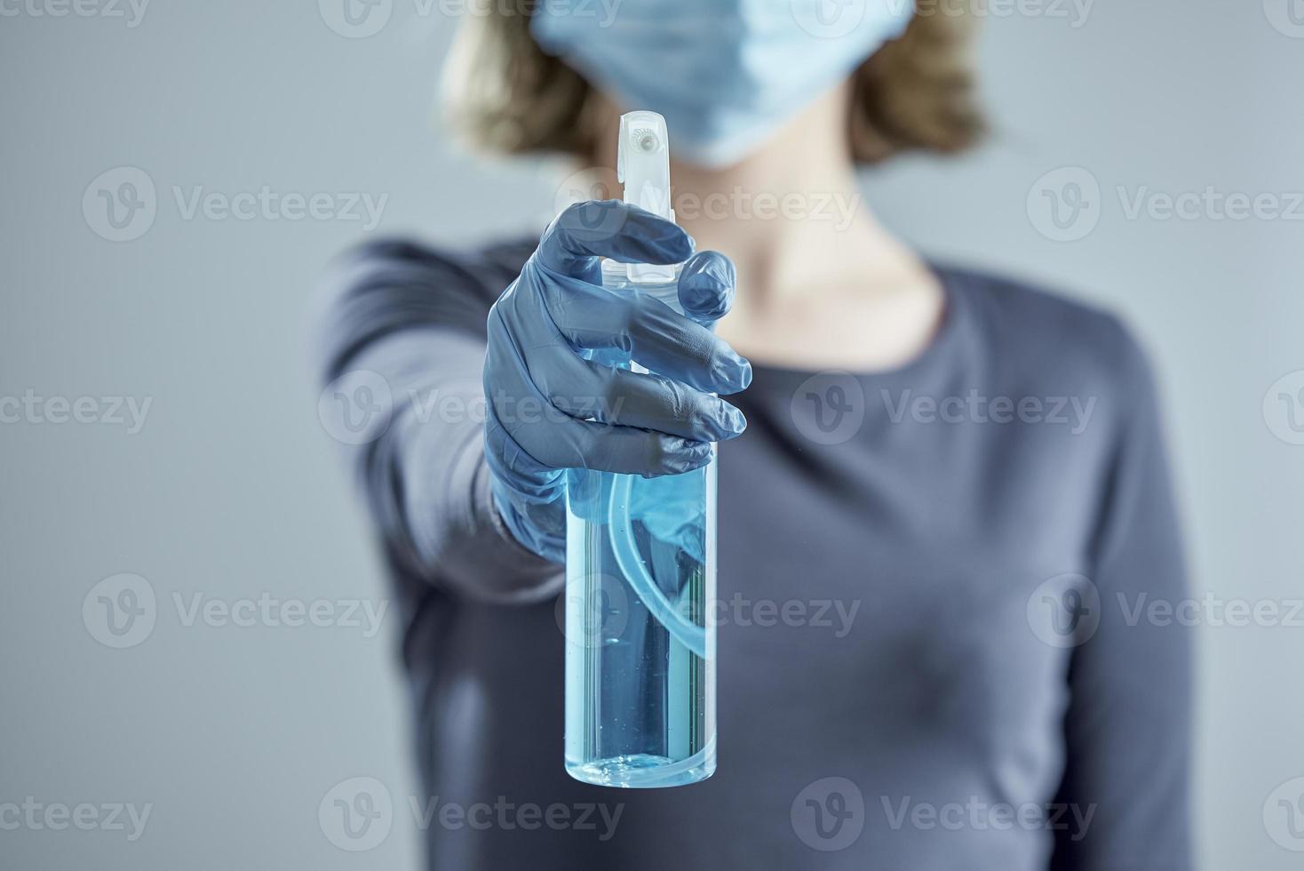 A girl in a medical mask and rubber gloves in blur holds out sanitizer. photo