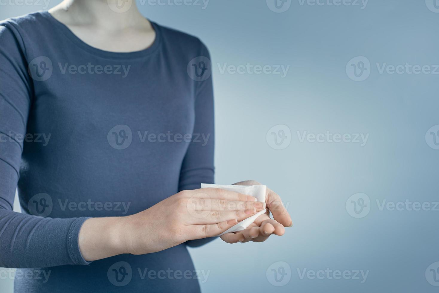 Young woman cleaning her hands by using white antibacterial napkin on gray background. Photo with copy space.
