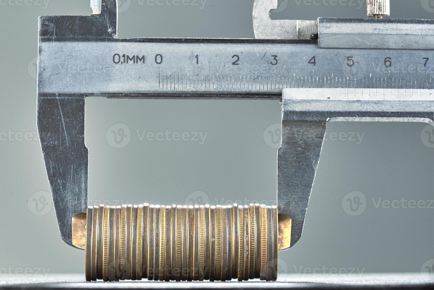 Calipers and stack of coins close-up against gray wall. photo