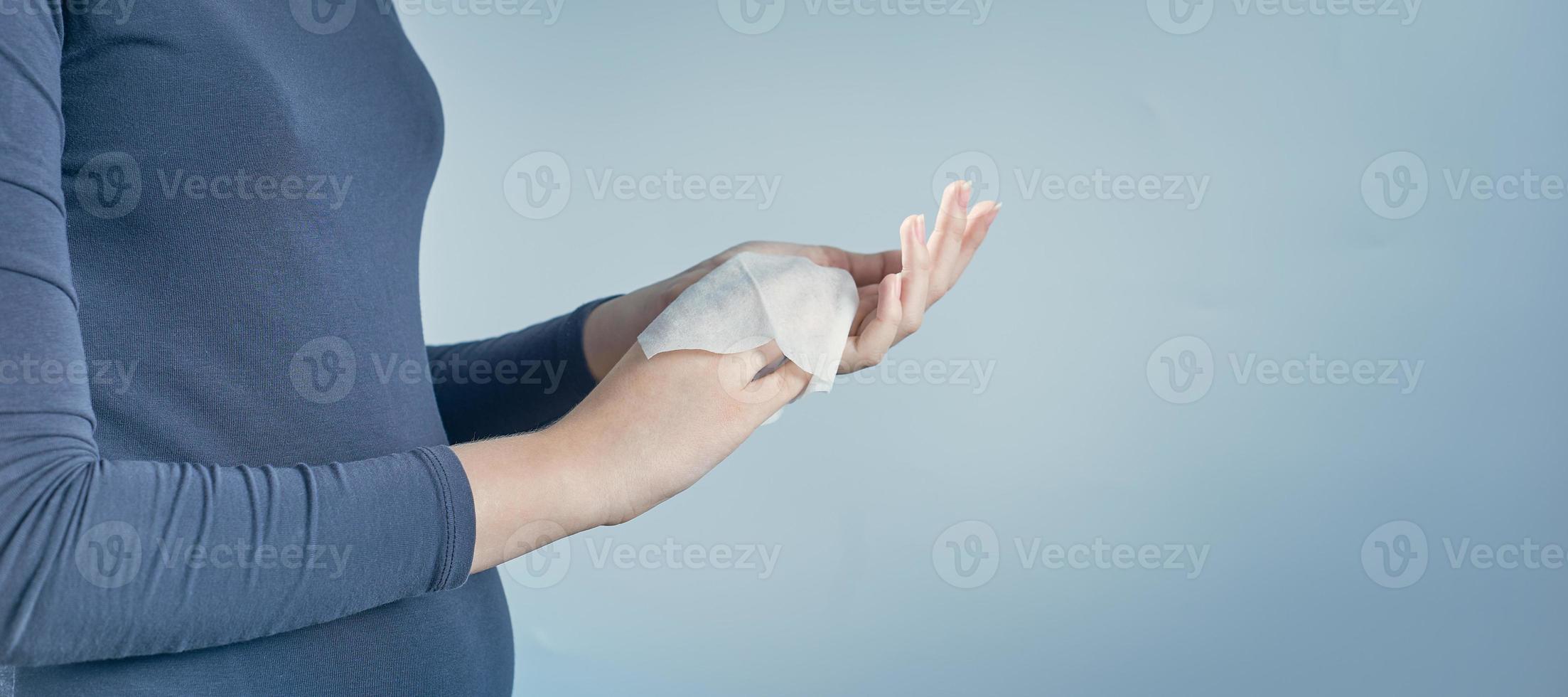 Girl cleaning her hands by using white antibacterial napkin on gray background. Photo with copy space.