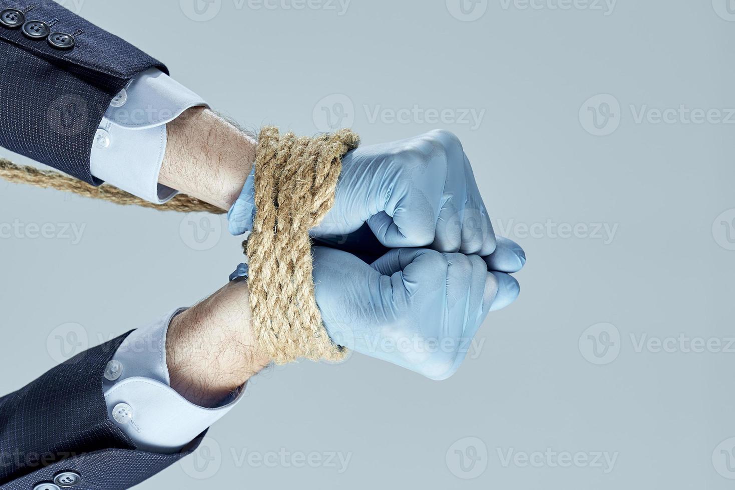Businessman's hands in rubber gloves are tied with a rope on gray background. Concept of a problem for business. photo