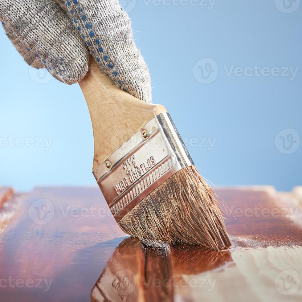 mano del hombre con un pincel pintando una superficie de madera sobre un fondo azul. foto