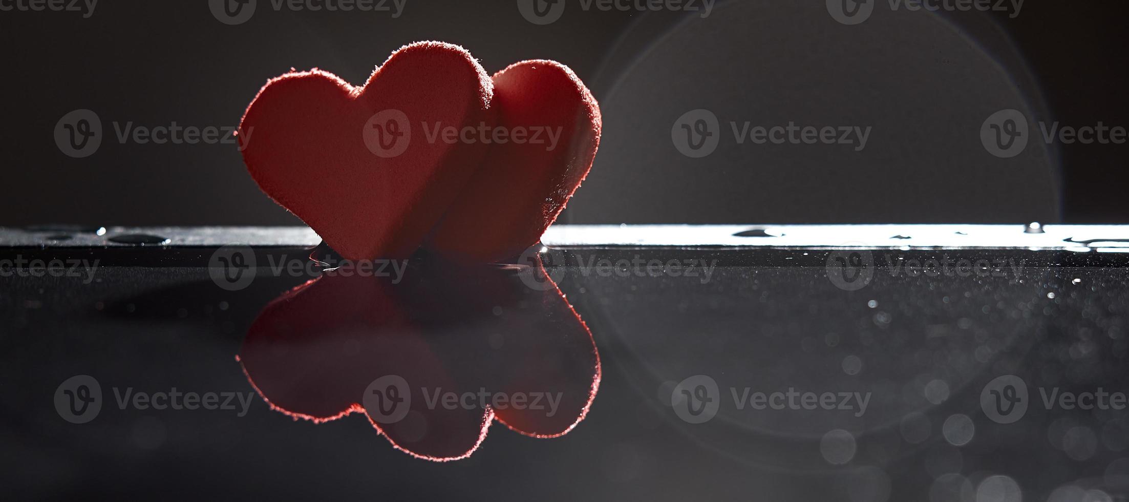 las siluetas de dos corazones rojos se reflejan en el agua sobre un fondo oscuro con un bokeh. foto con espacio de copia.