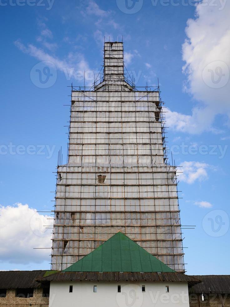 Scaffolding from planks around old bell tower. Background blue sky with clouds. photo