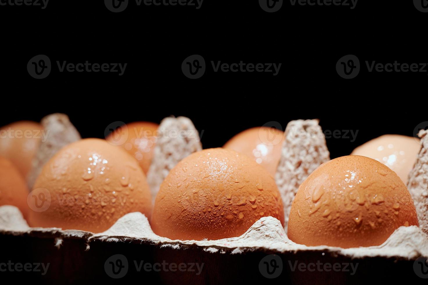 Eggs covered with water drops in a protective container on black background. photo
