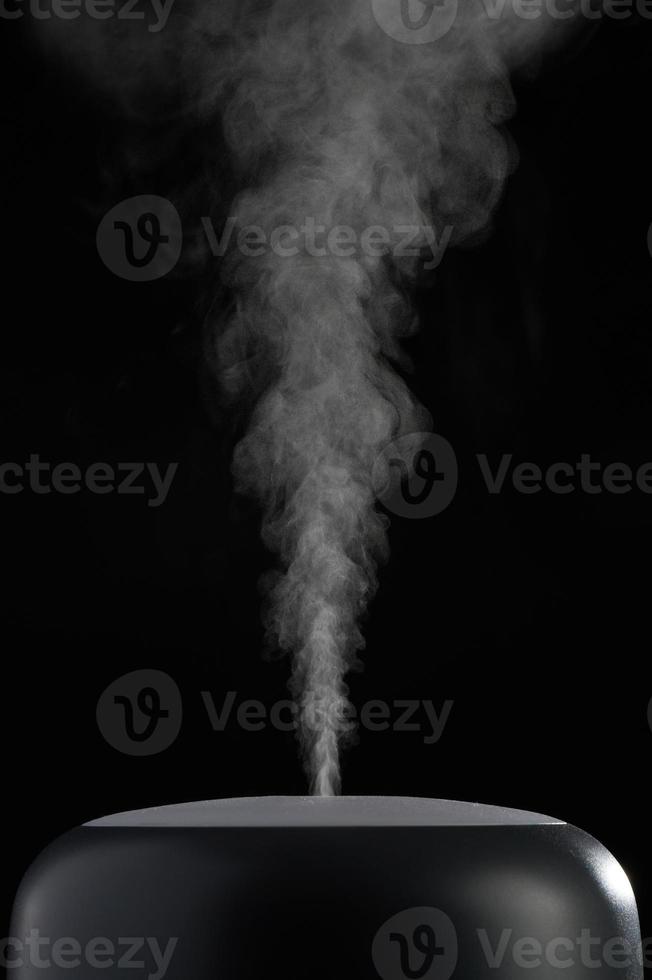 Modern air humidifier on black background. White steam close-up. The concept of humidification of the air. Photo with copy space.