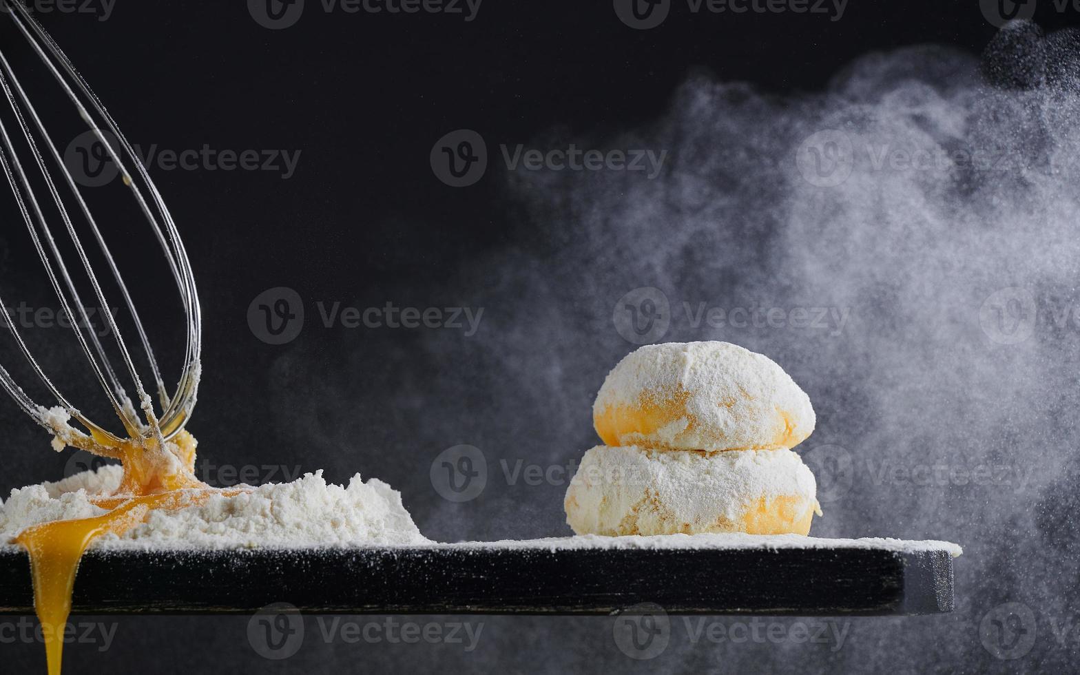 Raw dough sprinkled with flour and a whisk on a black background. Yeast dough for bread, rolls, pizza or pie. Copy space. photo