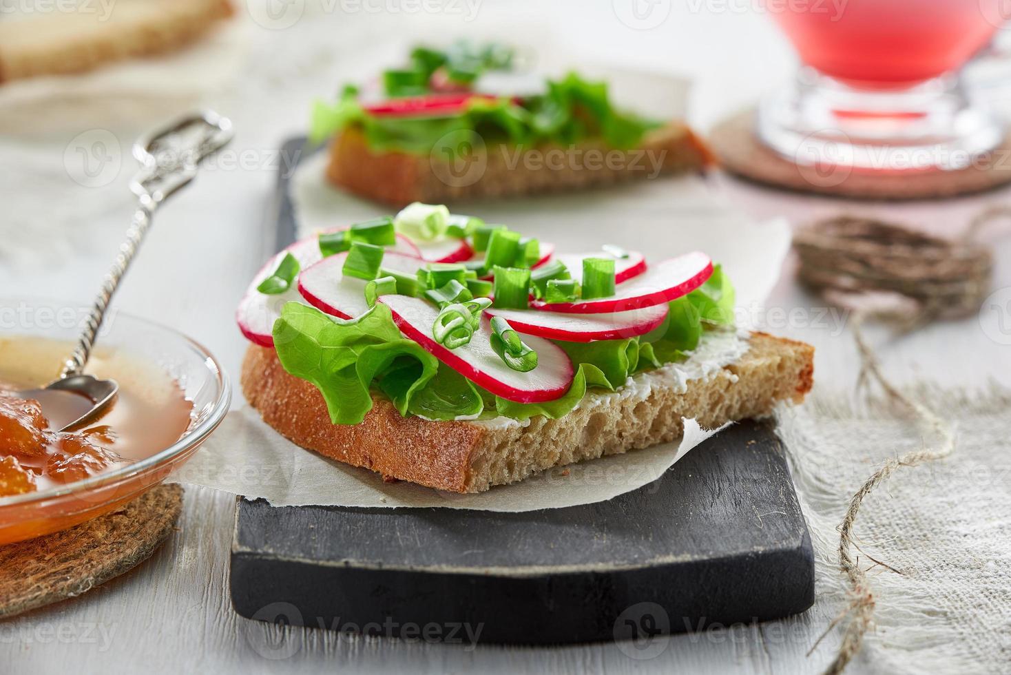 sándwich con requesón, rábano, cebolla verde y lechuga en una tabla de cortar. el concepto de desayuno saludable. foto