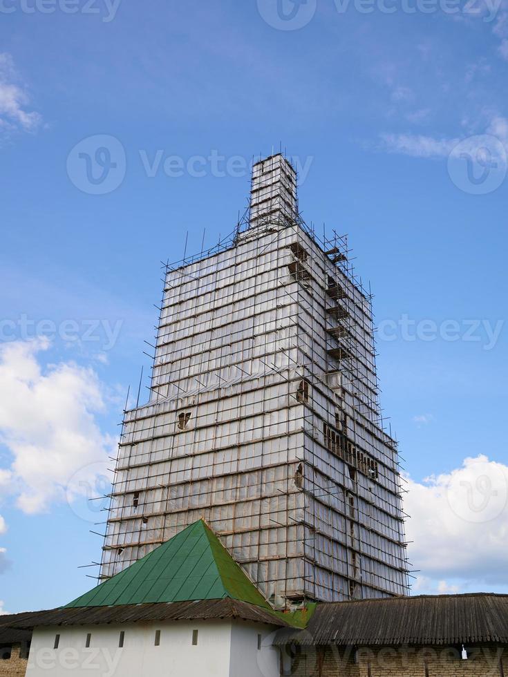 Scaffolding from planks around old bell tower. Background blue sky with clouds. photo