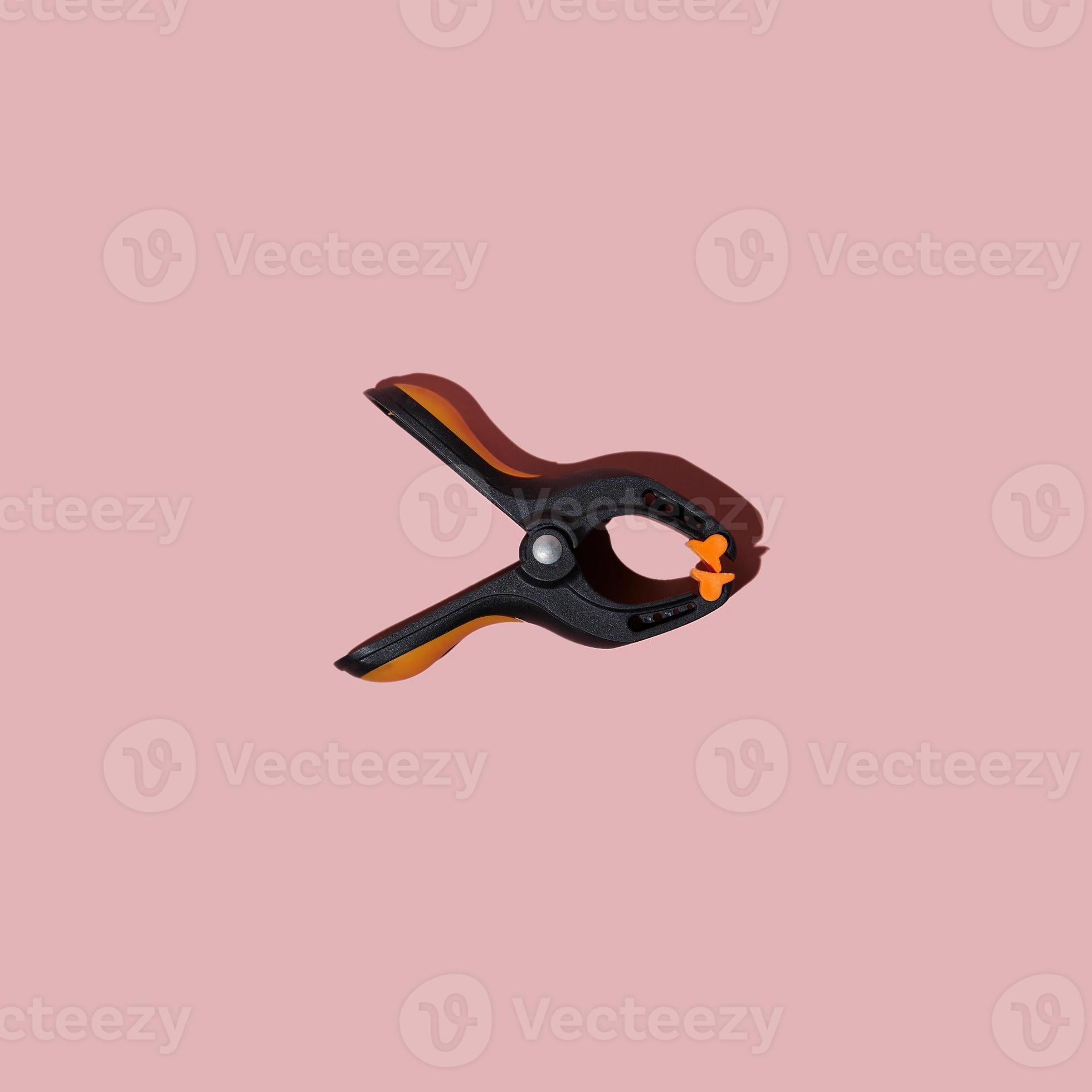 Plastic spring clamp isolated on pink background. Working hand tool. Black and orange spring