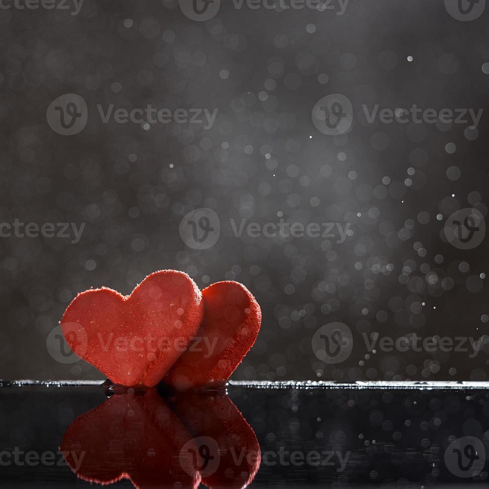 Two red hearts with rain drops reflected in the water on a dark background with a bokeh. Photo with copy space.