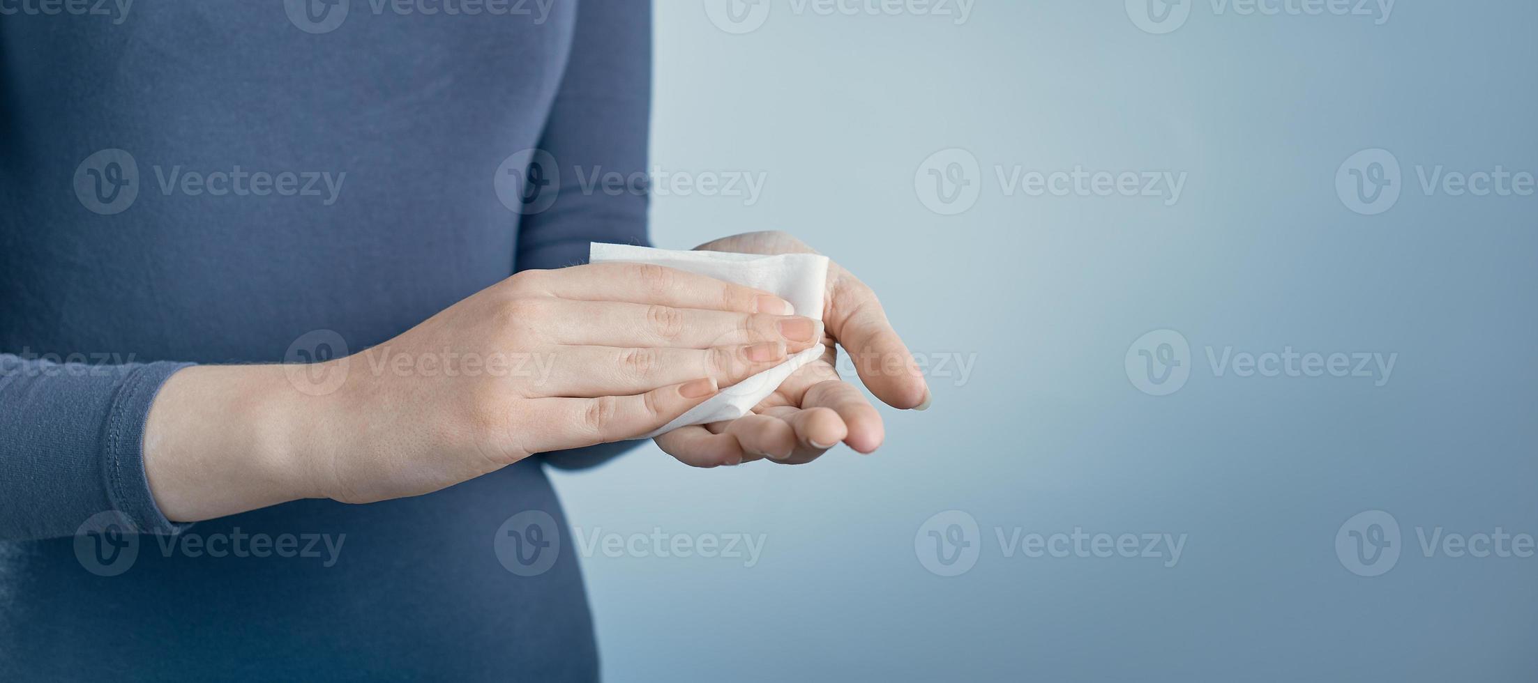 Girl cleaning her hands by using white antibacterial napkin on gray background. Photo with copy space.