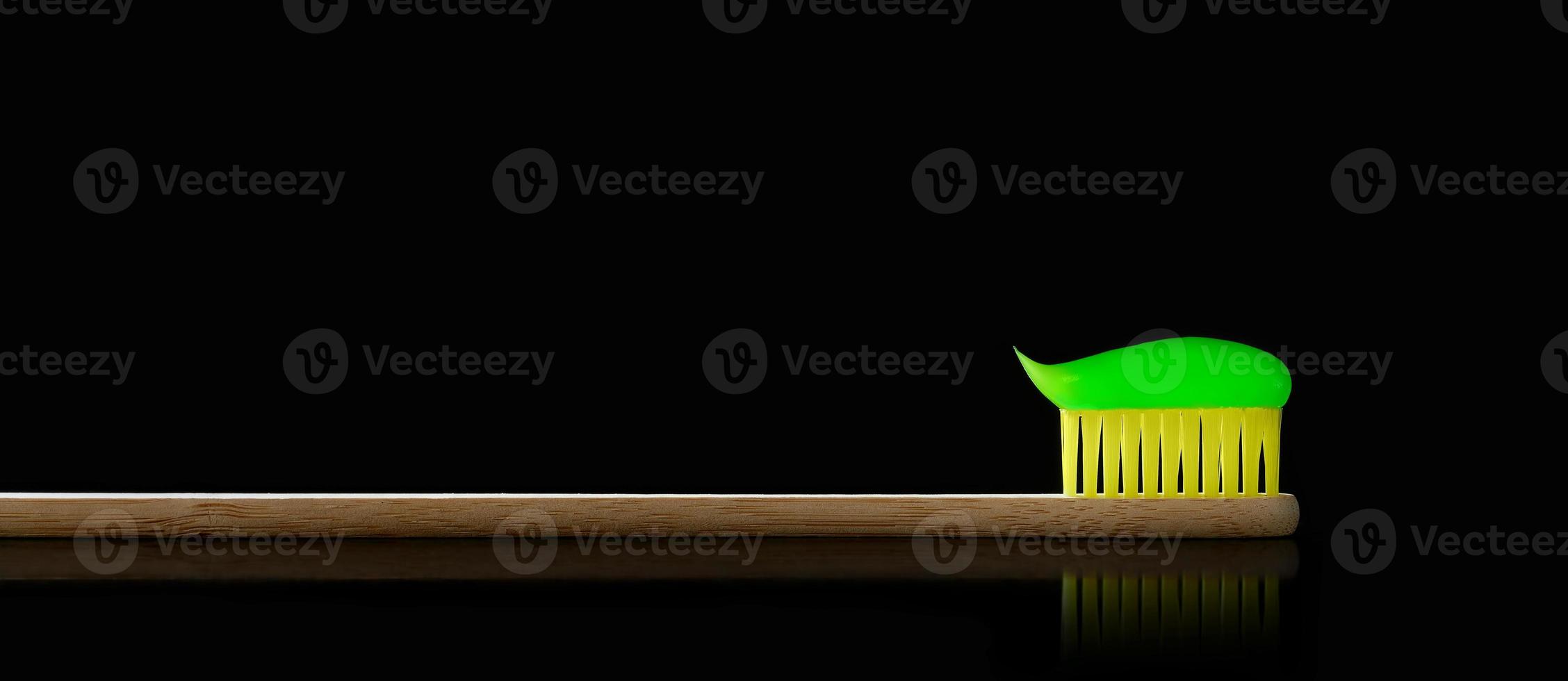 Natural bamboo toothbrush with reflection on black isolated background. There is green toothpaste on toothbrush. Photo with copy space.