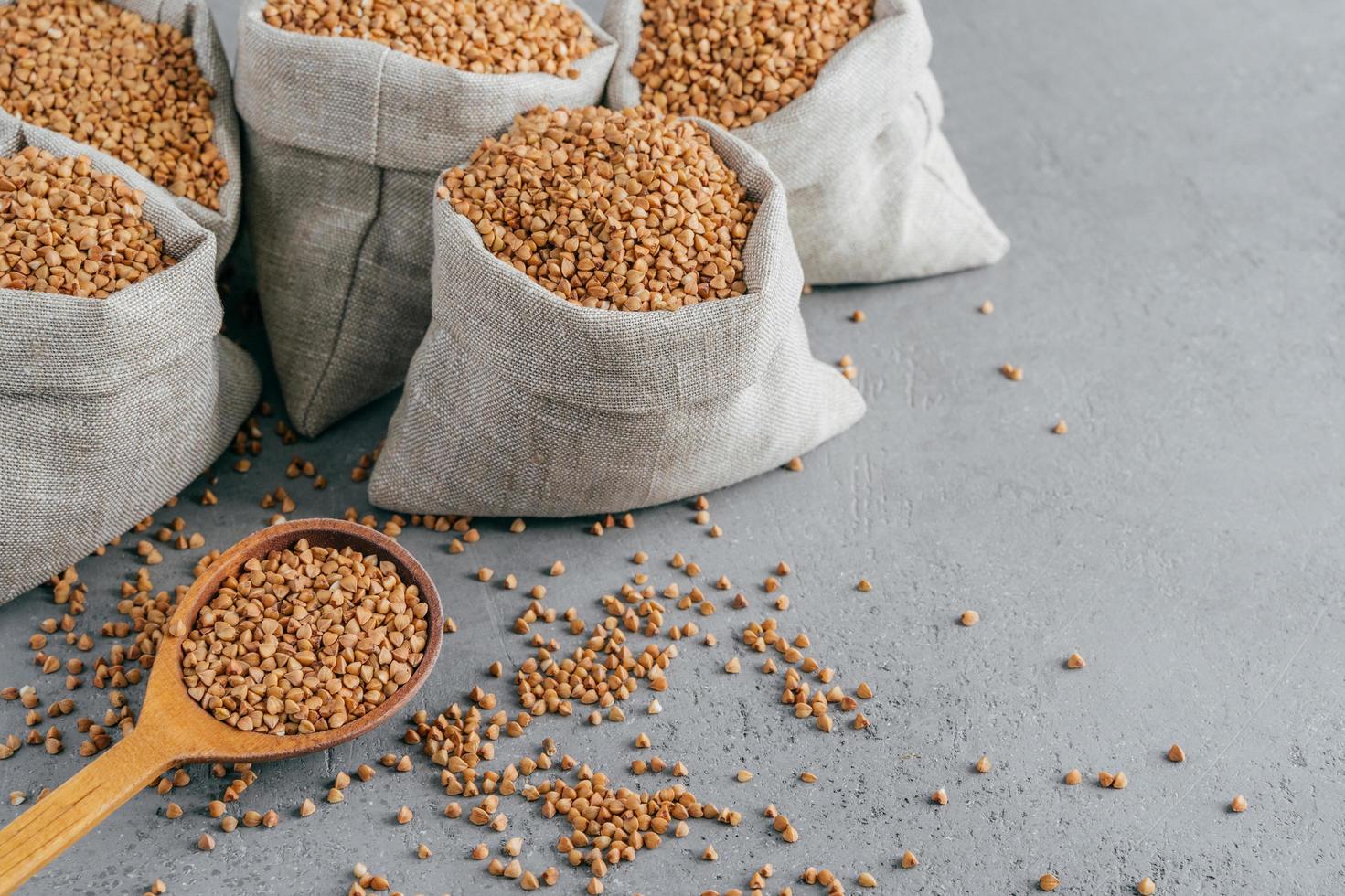 Eco food and clean eating concept. Buckwheat in small linen bags. Wooden spoon filled with protein product, Copy space on grey background. photo