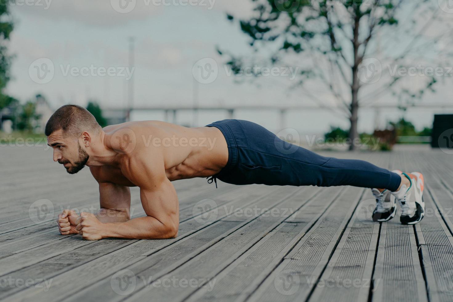 Motivated male athlete does abs exercise, enjoys bodybuilding training outdoor and stands in plank. Strong muscular European adult man has fitness workout. People and healthy lifestyle concept photo