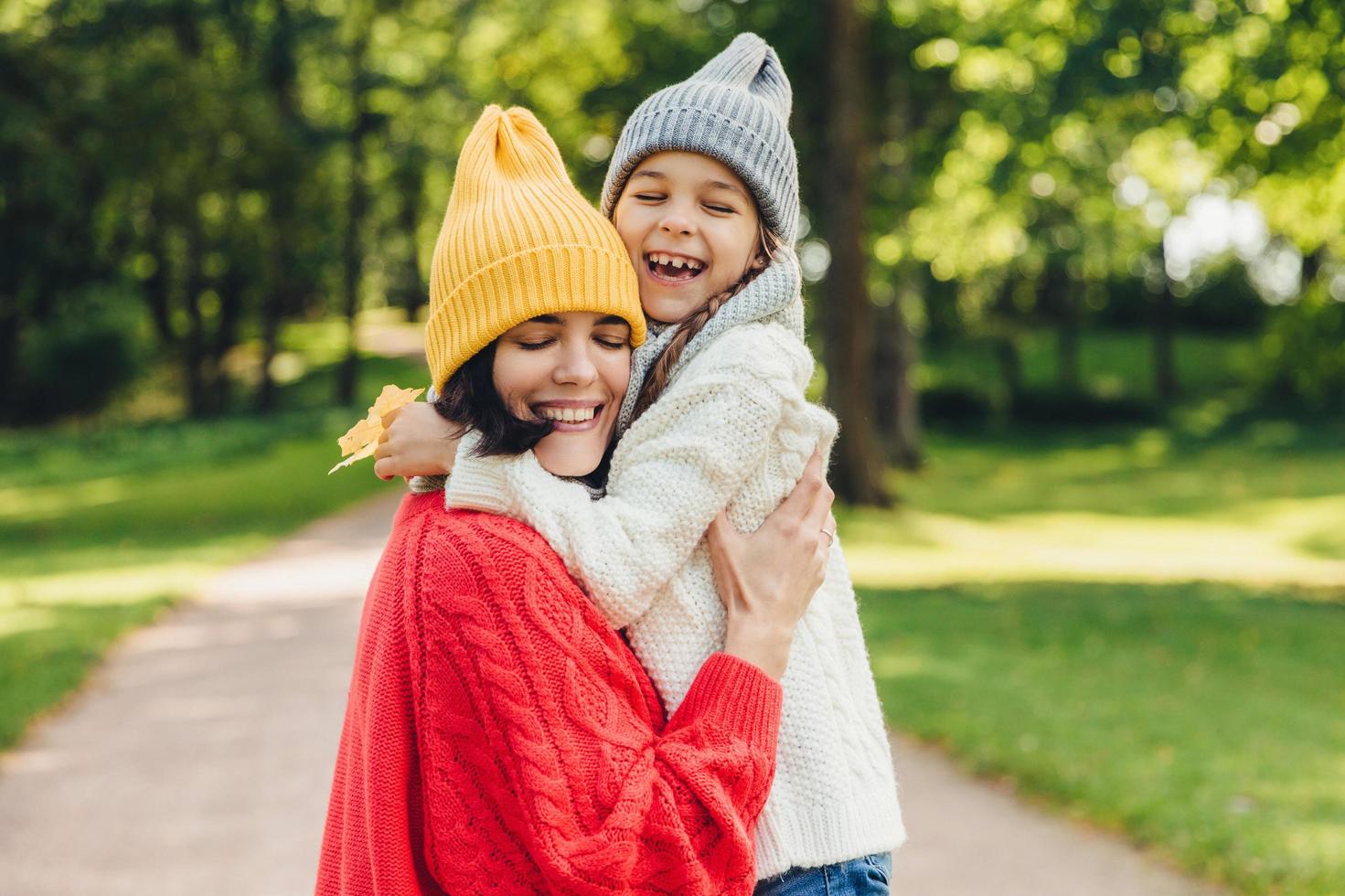 Parenthood, happiness and lifestyle concept. Beautiful female and her daughter have warm embrace, dressed in knitted clothes, have walk during autumn day, enjoy sunny weather, love each other photo