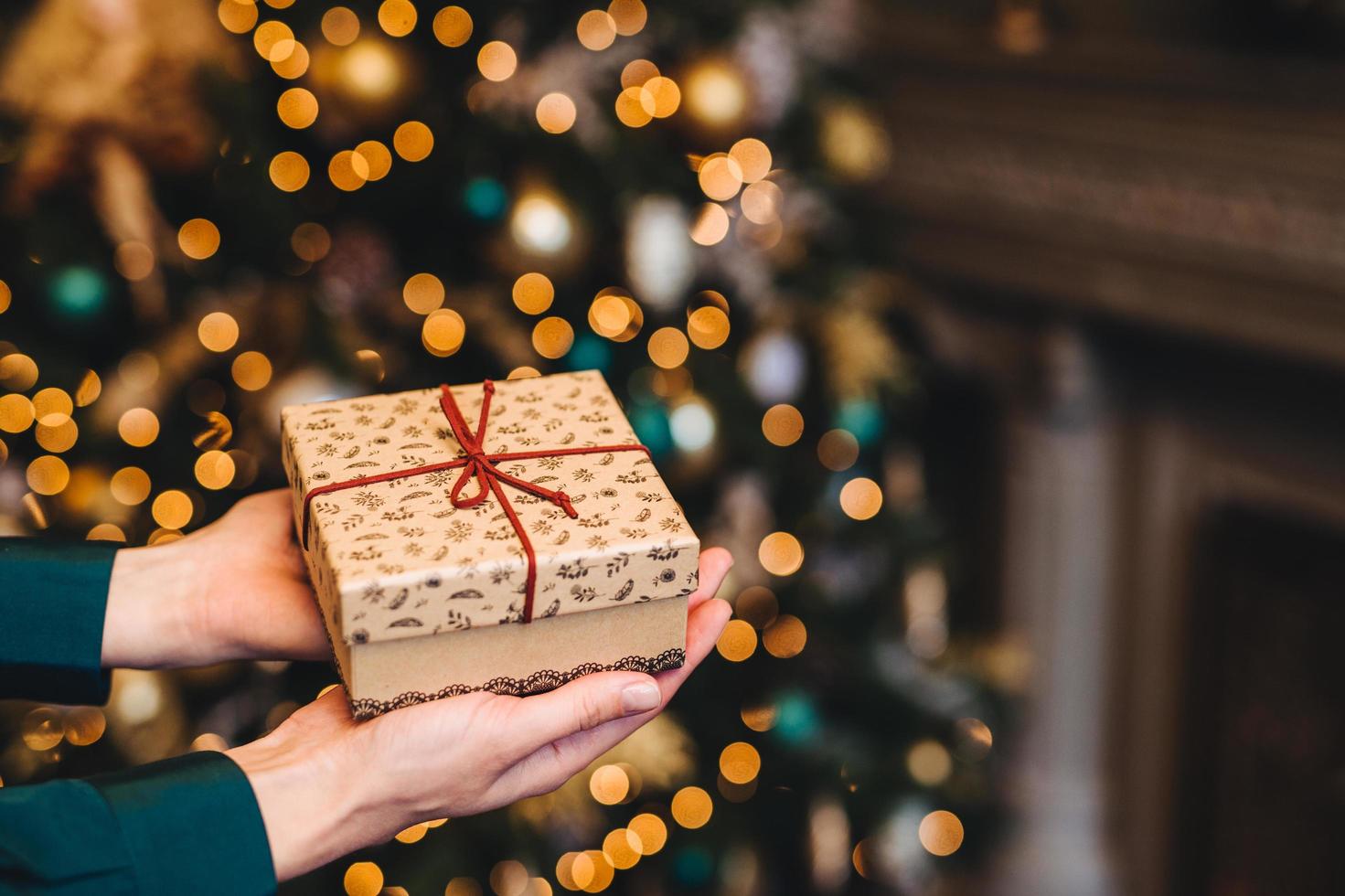 Hirizontal shot of beautiful wrapped present box in womans hands against decorated Christmas or New Year tree. New Year background. Focus on gift box. Celebration concept. photo