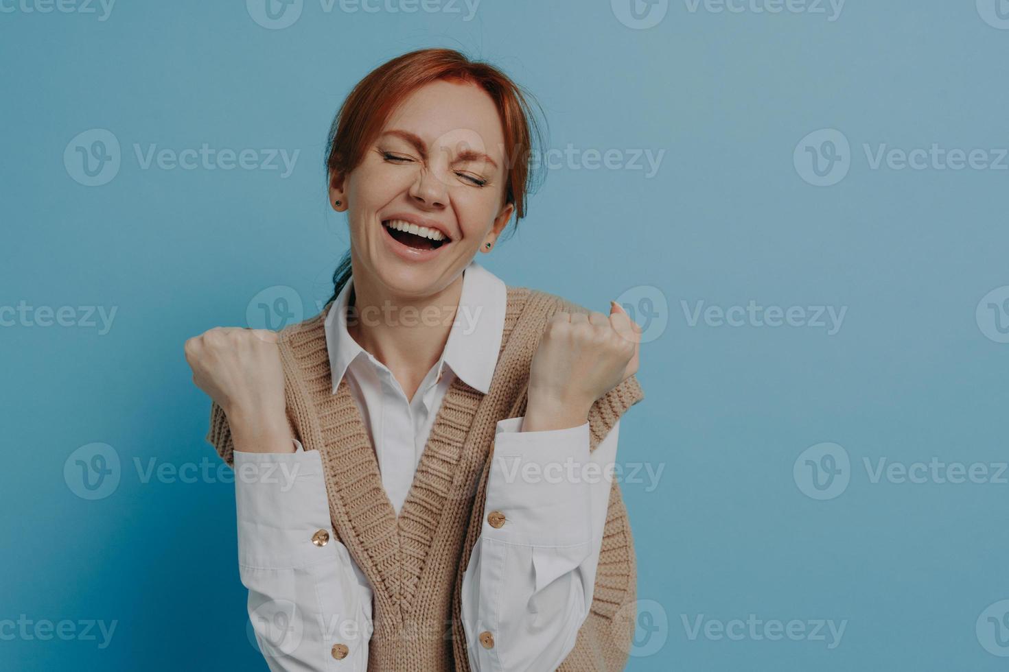Young happy satisfied young red haired woman with closed eyes celebrating success photo