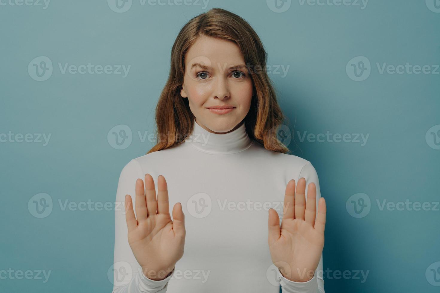 Attractive young focused woman showing stop gesture, saying no, isolated over blue studio background photo