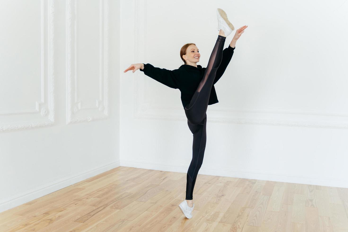 la mujer atlética en forma demuestra resiliencia, se equilibra en una pierna, es gimnasta deportiva experta, se viste con ropa deportiva y zapatillas de deporte, tiene ejercicios de pilates, se para en una sala vacía, tiene una figura hermosa foto