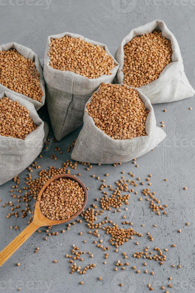 producto sin gluten. disparo vertical de trigo sarraceno marrón seco para vegetarianos. sacos con cereales. cuchara de madera cerca. concepto de alimentación saludable foto