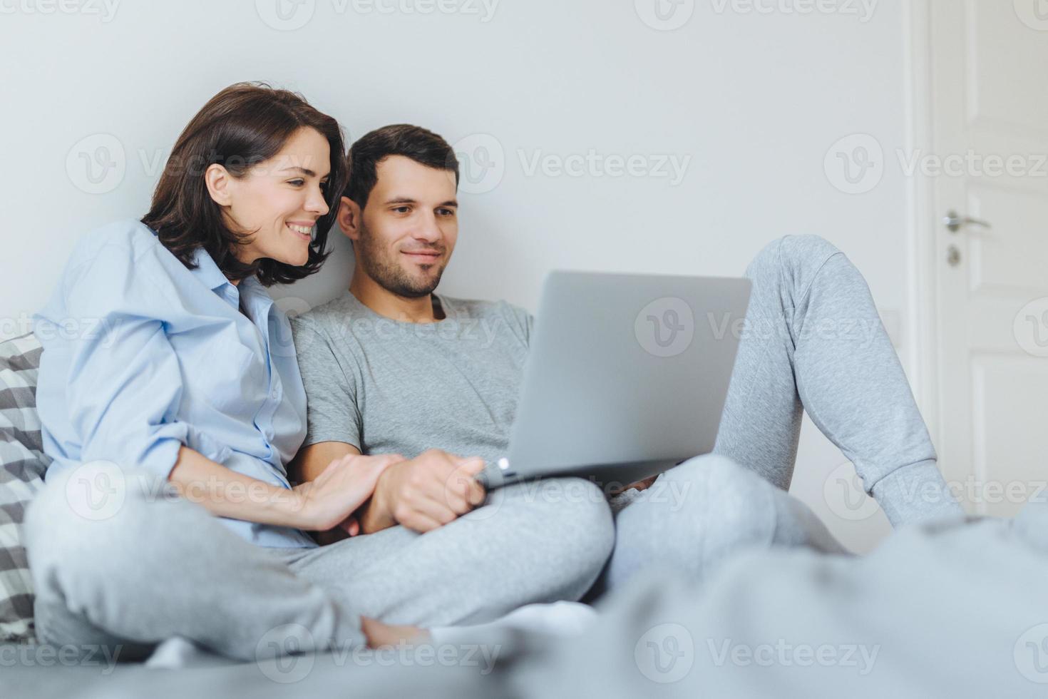 Happy couple in love review their wedding photos on laptop computer, remember plesant moments and special event in their life, use modern laptop computer and free internet connection at home