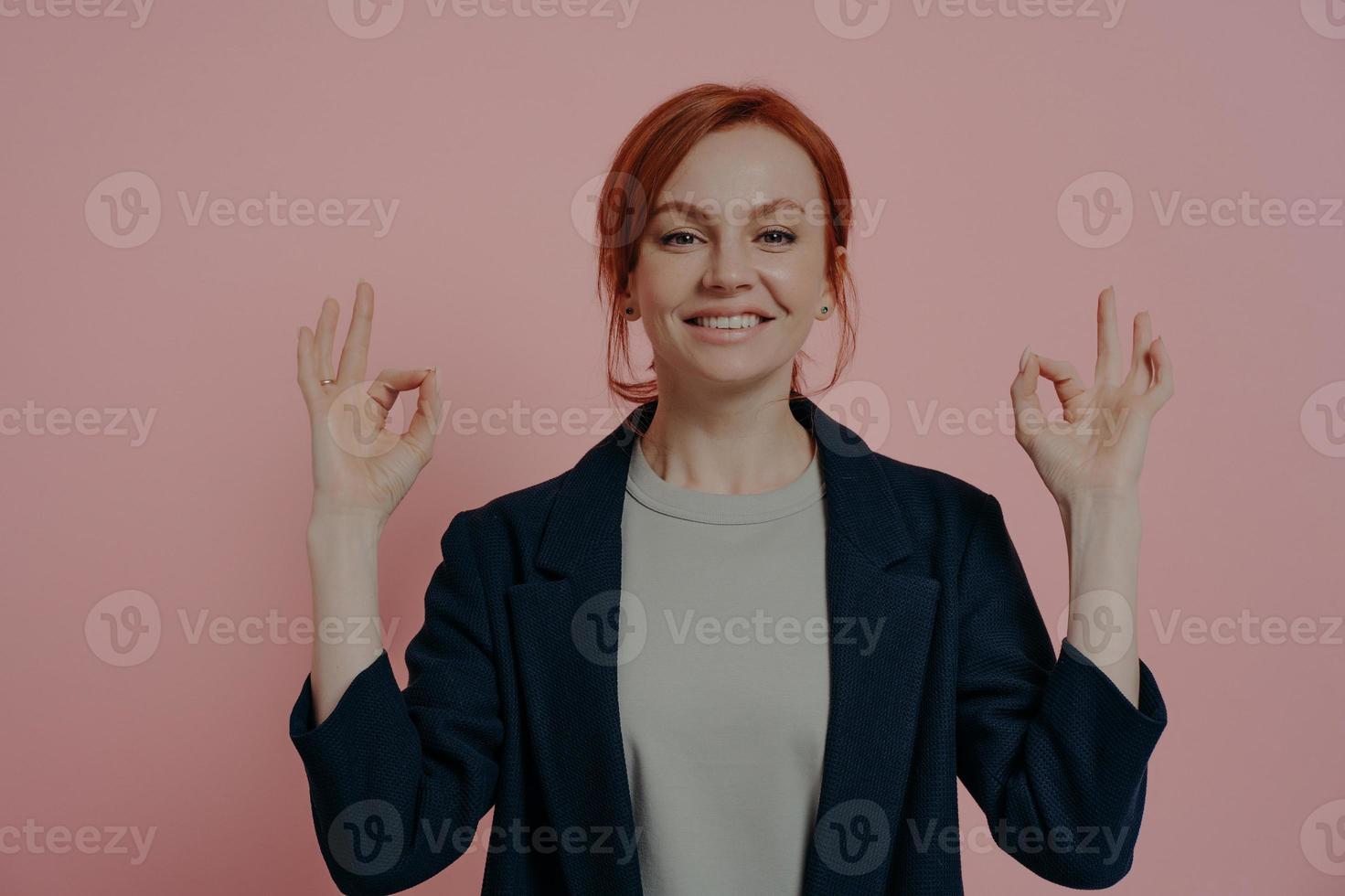Studio portrait of calm peaceful red-haired business woman with mudra hands gesture photo