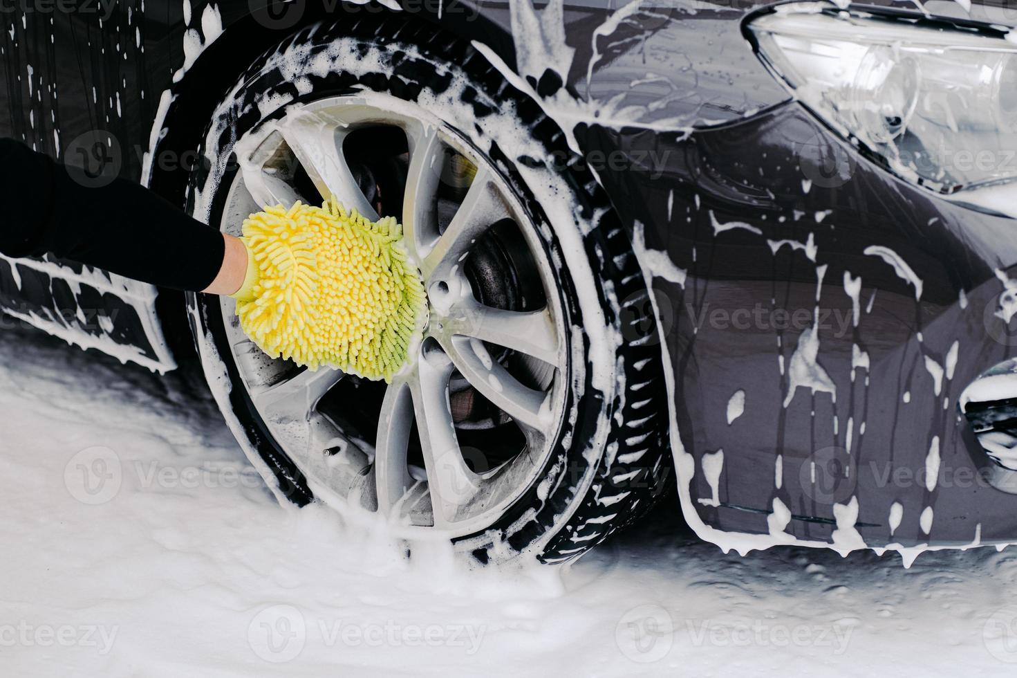 Workers hand with yellow sponge washing car wheels with detergent for cleaning vehicles. Maintenance and service concept photo